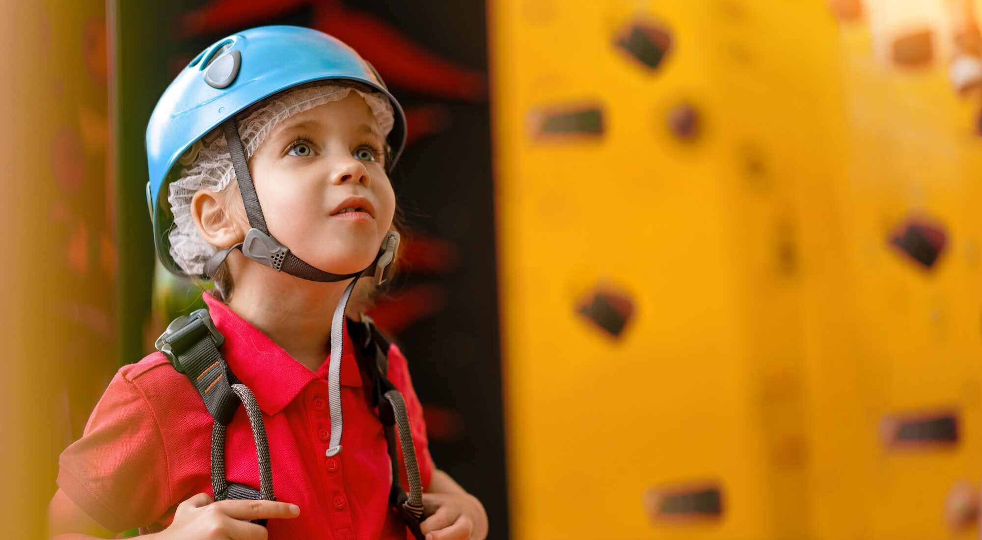 Child climbing on wall in amusement centre. Climbing training for children. Little girl helmet